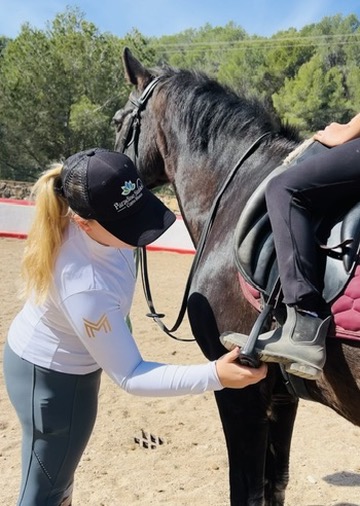 Instructor adjusting a rider's stirrup on a black horse in the arena