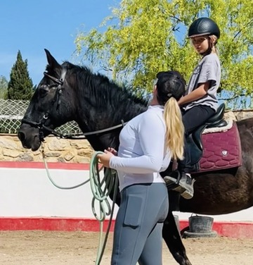 Instructor leading a young rider on a black horse during a private lesson in the arena