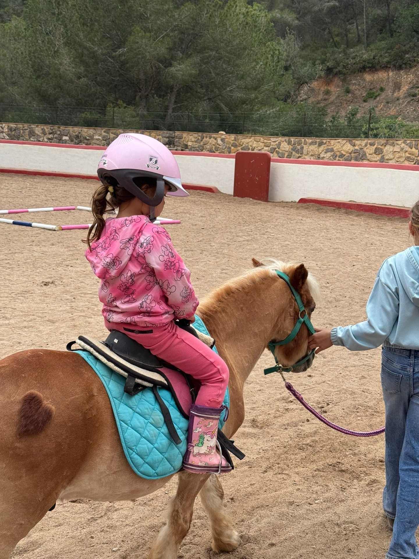 Young child being led on a small pony during a beginner lesson in the arena