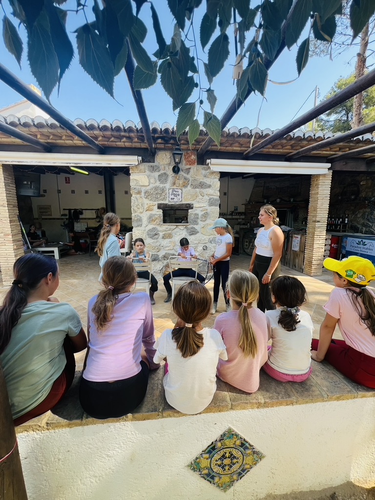Group of children learning horsemanship theory in a shaded circle at Paradise Stables