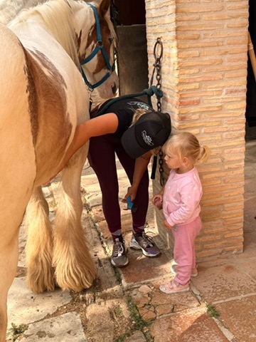 Instructor showing a toddler how to groom a pony at Paradise Stables
