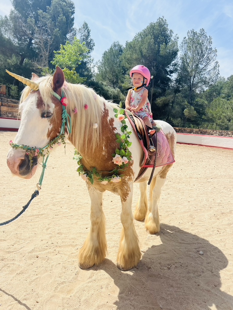 Toddler in a pink helmet on a decorated unicorn pony at Paradise Stables